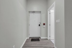 A hallway with a white door, a fire alarm, and a mat on the floor.