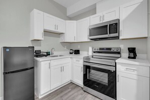 A modern kitchen with white cabinets, stainless steel appliances including a refrigerator, microwave, and oven, and a coffee maker.