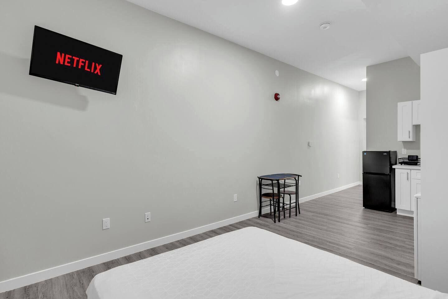 A modern apartment with a kitchenette, a dining area with a table and chairs, and a large flat-screen TV mounted on the wall.