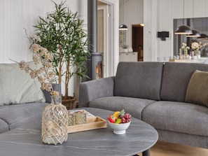 A modern living room with a grey sofa, a round coffee table with a bowl of fruit, a potted plant, and a decorative vase. - 16 Person Holiday Home in Albaek (Aalbaek)