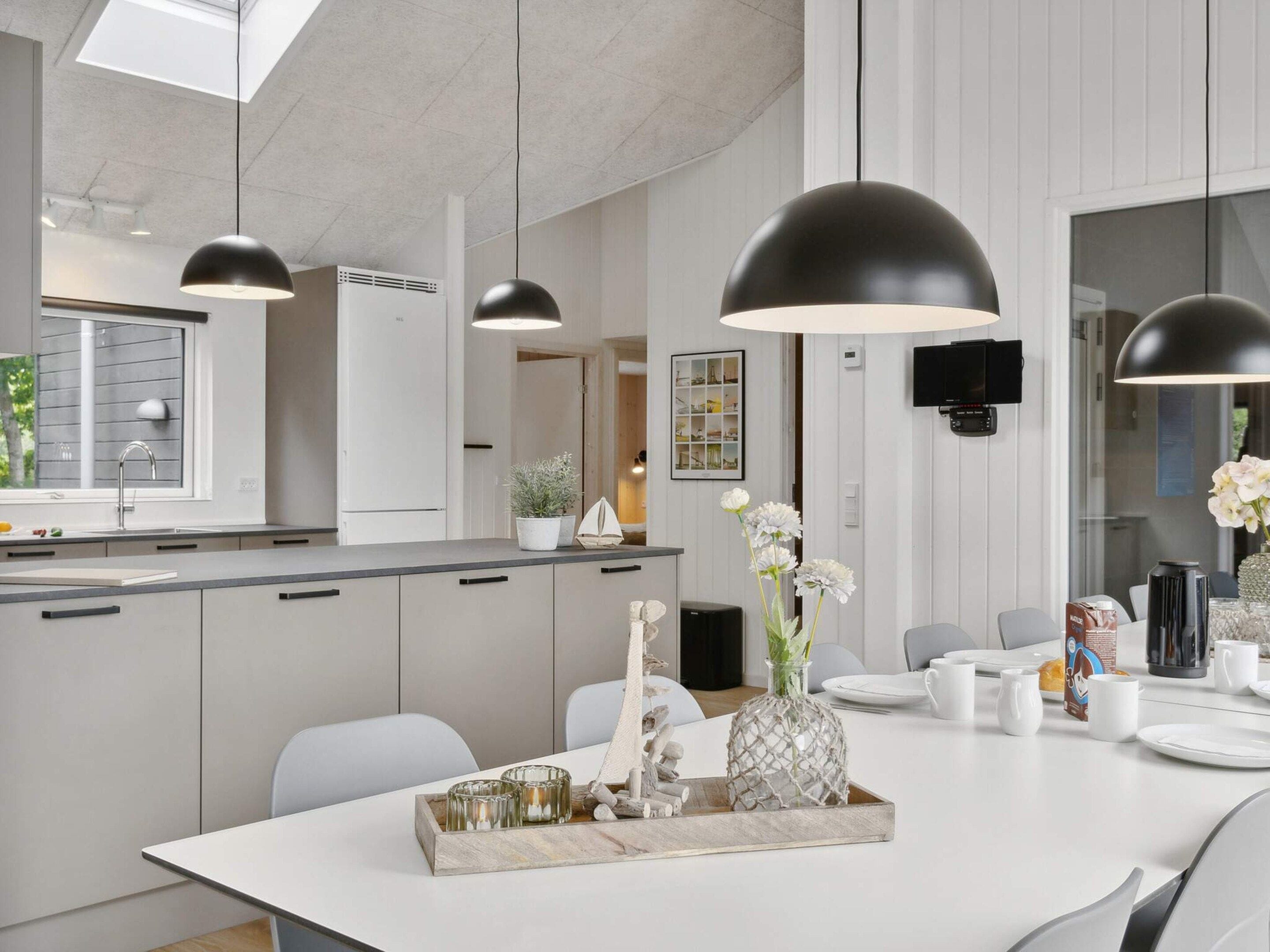 A modern kitchen with pendant lighting, a dining area with a white table, and a view of the outdoors.
