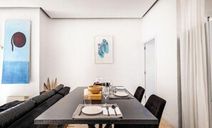 Ein Essbereich mit einem langen Tisch, gedeckt für vier Personen, einer schwarzen Couch und zwei gerahmten Kunstwerken an der Wand.