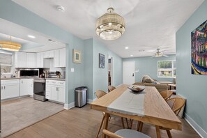 A modern kitchen with white cabinets, a stainless steel range, and a dining area with a wooden table and wicker chairs. - Spacious 4-bedroom house in charming Mary Esther (Mary Esther)