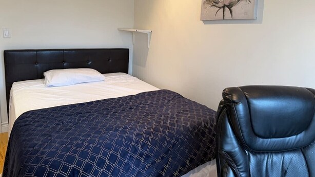 Un dormitorio con una cama, un sillón de cuero negro, una lámpara de pared y un cuadro.