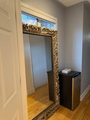 A room with a large ornate mirror, a black cabinet, and a door leading to another room.