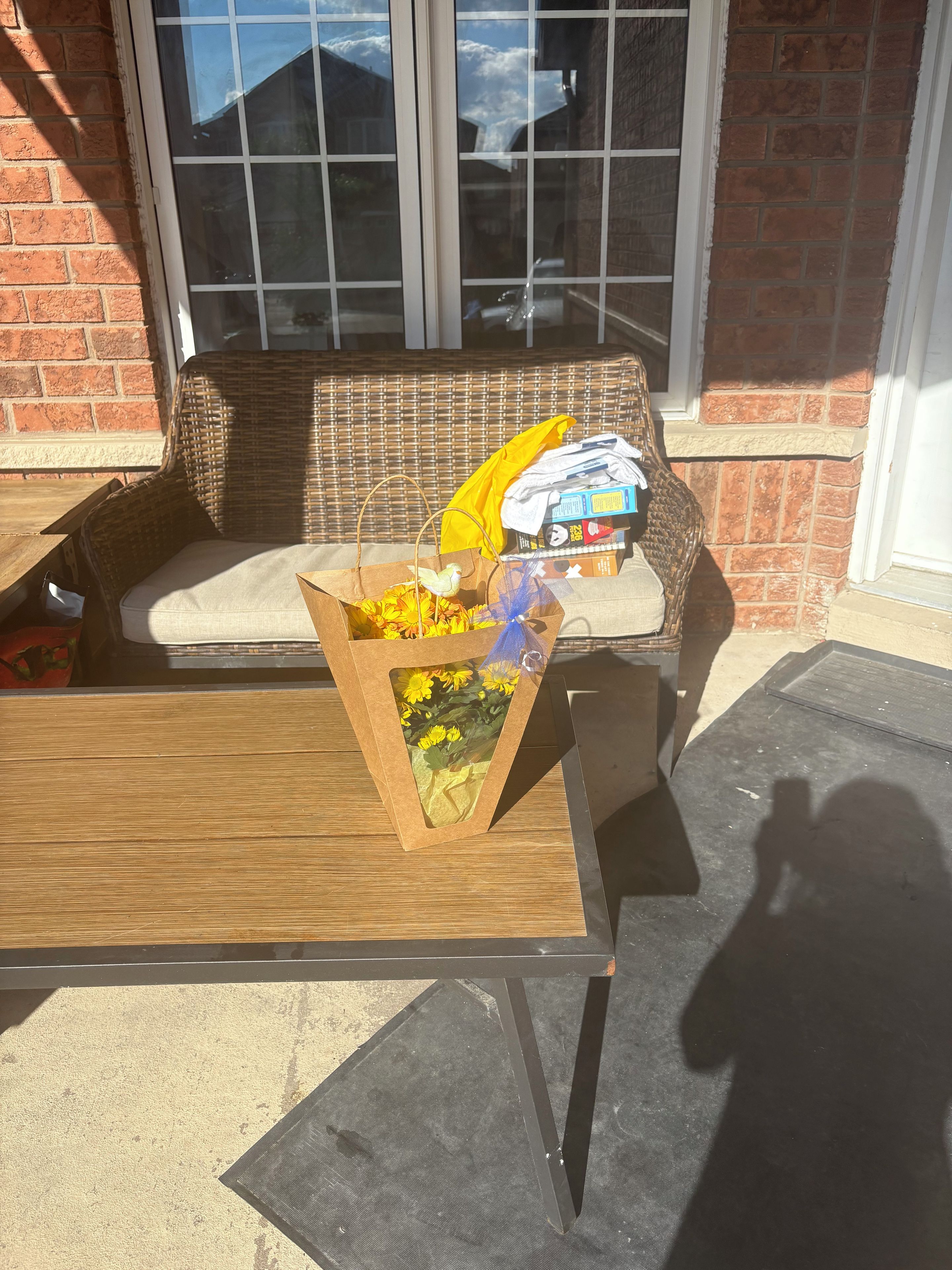 A wicker sofa with a cushion, a wooden table, and a cardboard box with yellow flowers.