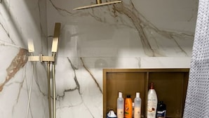 Ein Badezimmer mit Marmorwand, goldener Dusche und Ablage für Toilettenartikel.