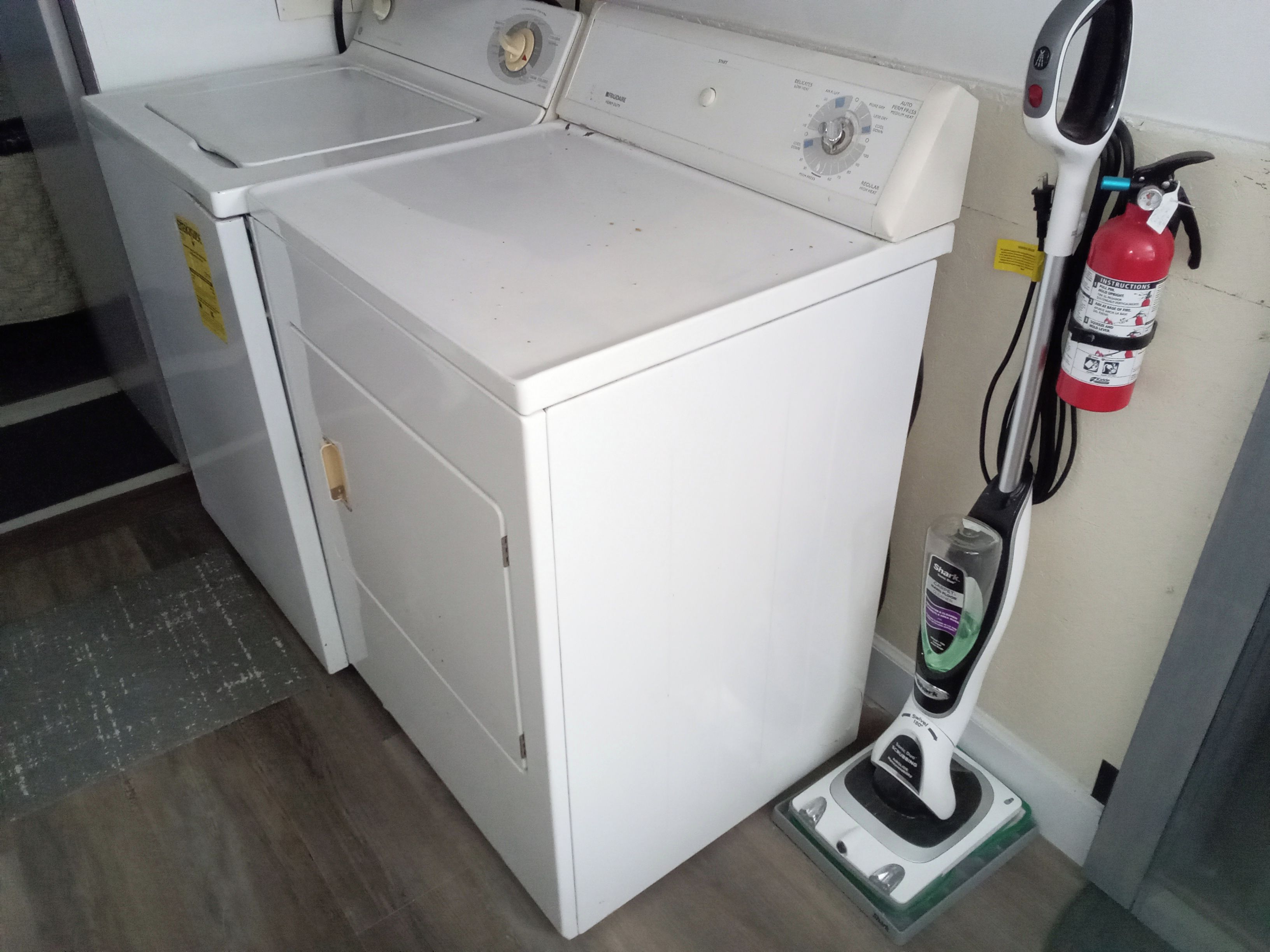 A front-loading washing machine with a control panel, a fire extinguisher, and a vacuum cleaner.