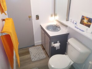 A bathroom with a white toilet, a sink with a mirror above it, and a small window with a view of palm trees. - Keaton Beach Lodge, serene, private parking for several towing vehicles & boats (Perry)