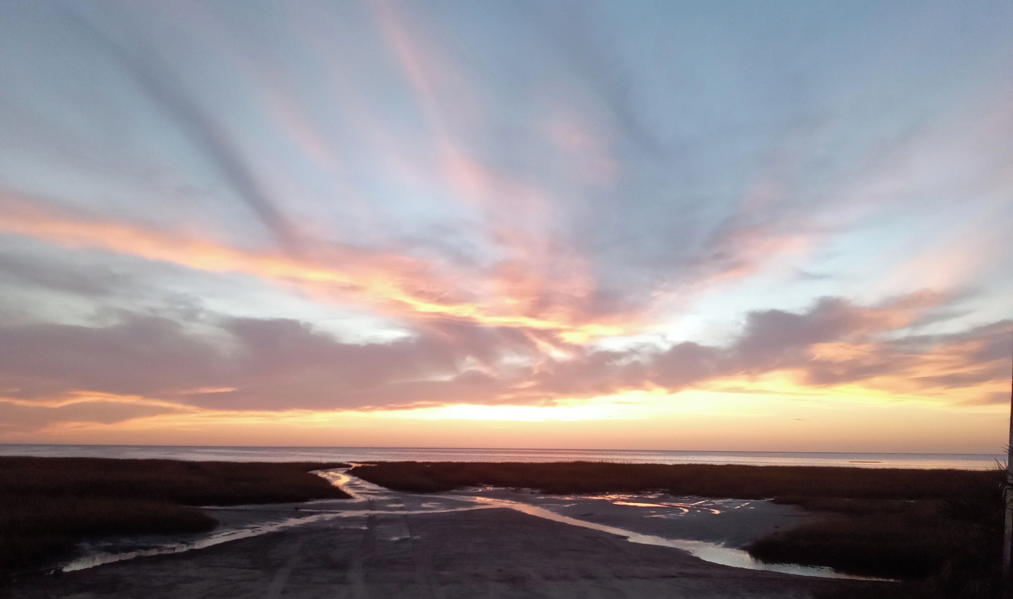 A sunset over a beach with a path leading to the water.