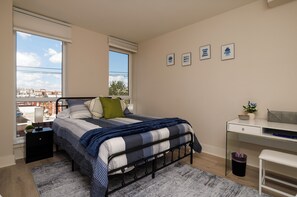 Una camera da letto con un letto, una scrivania e una finestra vista città.