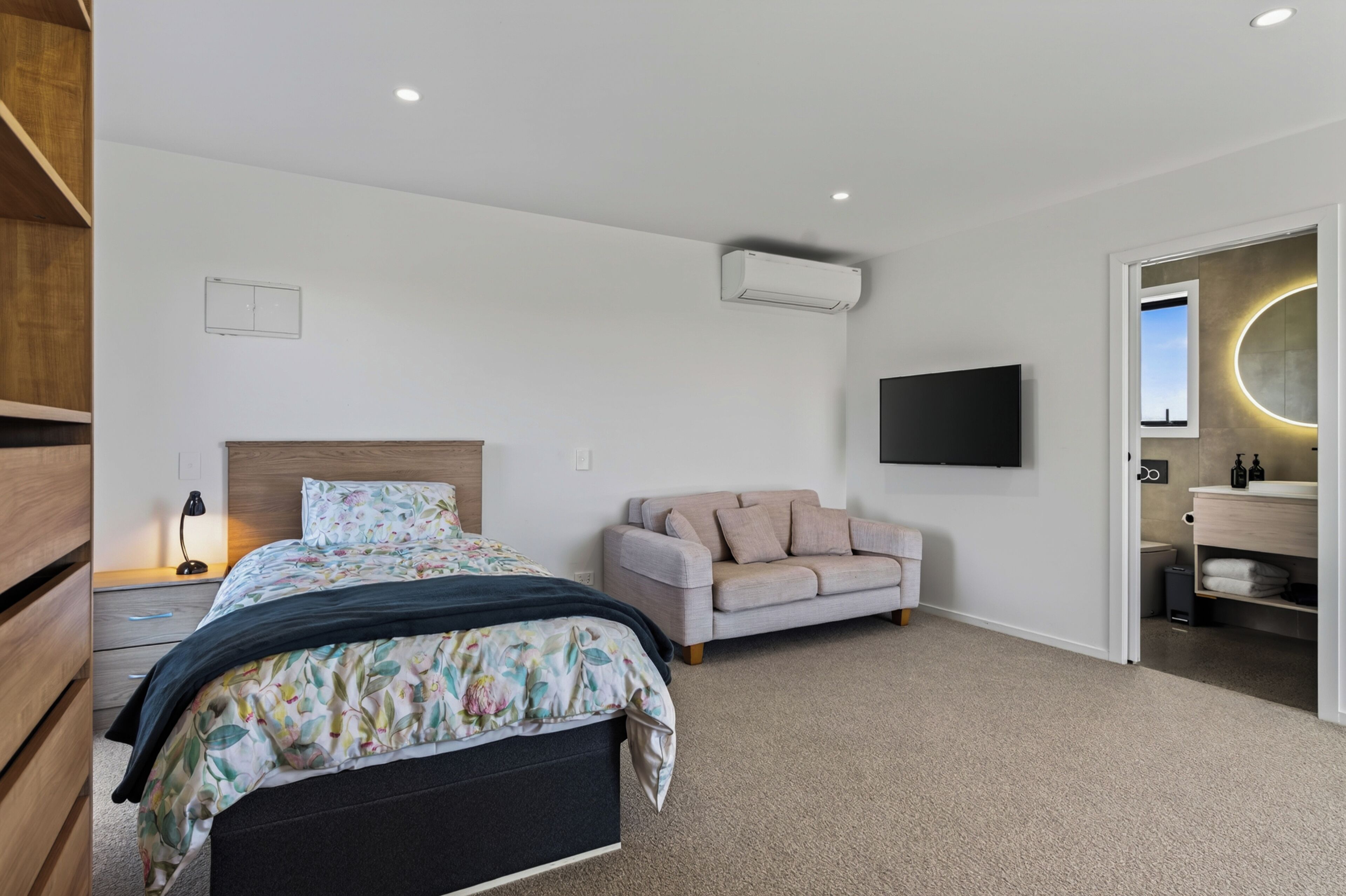 A modern bedroom with a bed, a sofa, a TV, and an air conditioning unit.