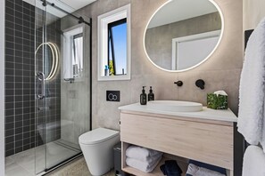 Een moderne badkamer met een douchecabine van glas, een wit toilet, een wastafel met een ronde spiegel en een handdoekhouder.