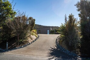 Une allée pavée mène à un bâtiment moderne doté d’un toit plat, qui est entouré de divers arbres et arbustes.