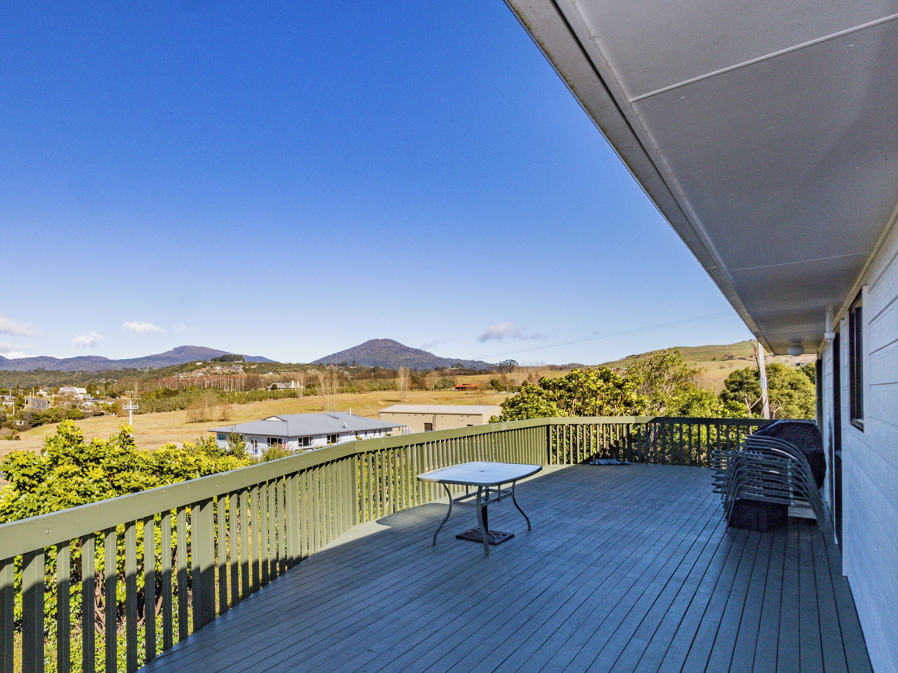 Eine Holzterrasse mit Tisch und Stühlen, mit Blick auf eine Landschaft mit Hügeln und Gebäuden.