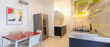 Cocina compacta con comedor, refrigerador, estufa y lámpara de pared.