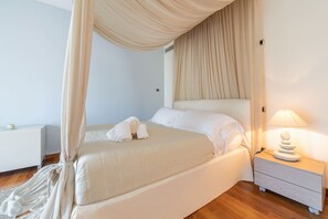 Een slaapkamer met een hemelbed, een nachtkastje met een lamp en een klein nachtkastje met een kaars.
