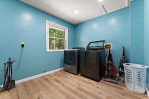 A laundry room with a washing machine, dryer, and vacuum cleaner against a blue wall. - Spacious 5BR Retreat in Peaceful Michigan City (Michigan City)
