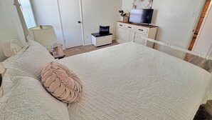 Un dormitorio con cama, televisor en una cómoda, una puerta y una ventana.