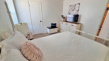 A bedroom with a bed, a television on a dresser, a door, and a window.