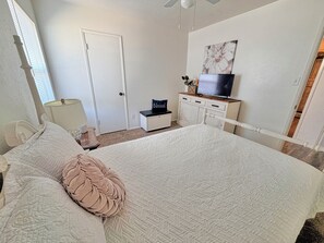 Une chambre à coucher avec un lit, un téléviseur posé sur une commode, une porte et une fenêtre.