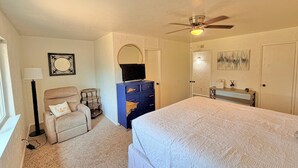 Un dormitorio con cama, cómoda, silla, escritorio, ventilador de techo y ventana.