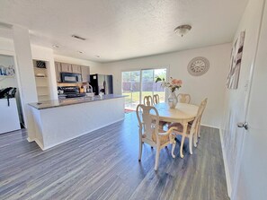 Une cuisine moderne avec un îlot central, une table à manger avec des chaises et une vue sur le jardin arrière.
