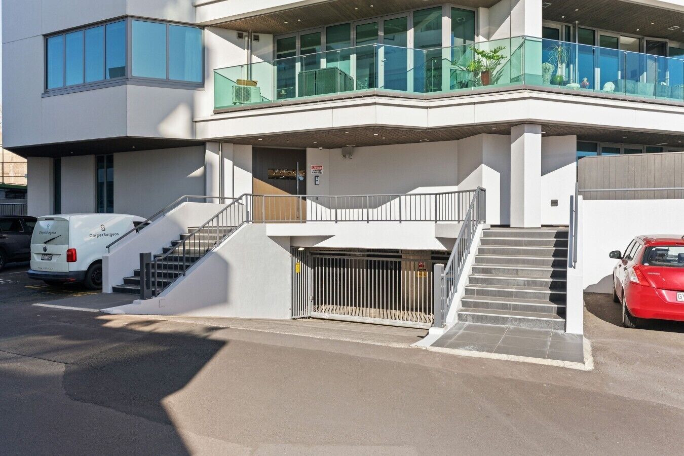 Un bâtiment moderne doté d’une entrée couverte, d’un escalier et d’une voiture garée devant.