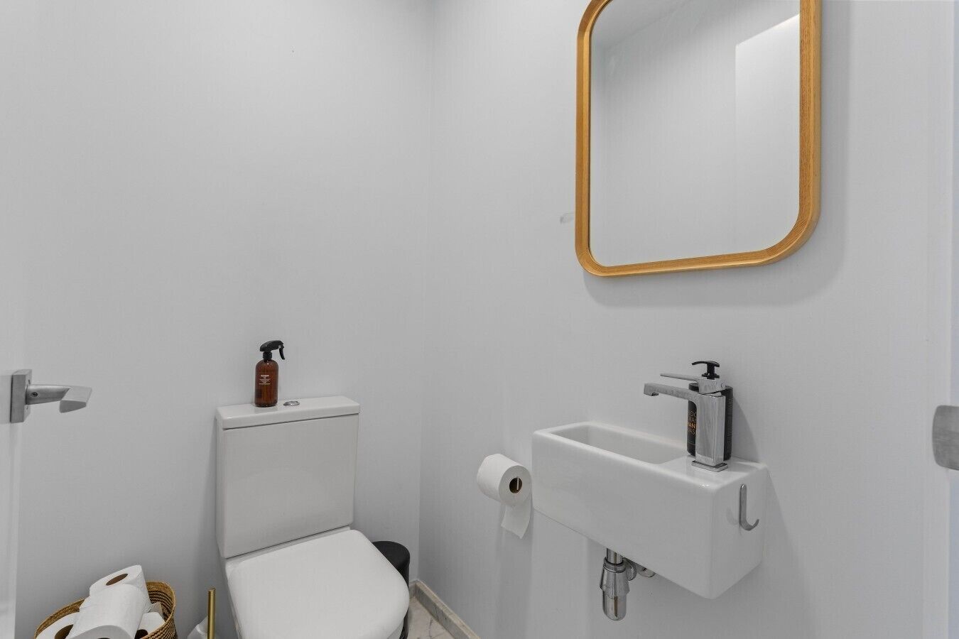 A bathroom with a toilet, a sink, a mirror, and a toilet paper holder.