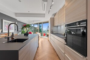 A modern kitchen with a central island, built-in appliances, and a view to the outdoors. - The Margot by Homello | Designer Apartment | Sky Tower Views | Ponsonby (Freemans Bay)