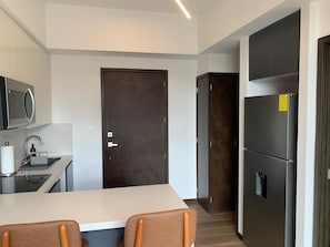 Una cocina moderna con encimera blanca, electrodomésticos de acero inoxidable y una puerta de madera oscura.