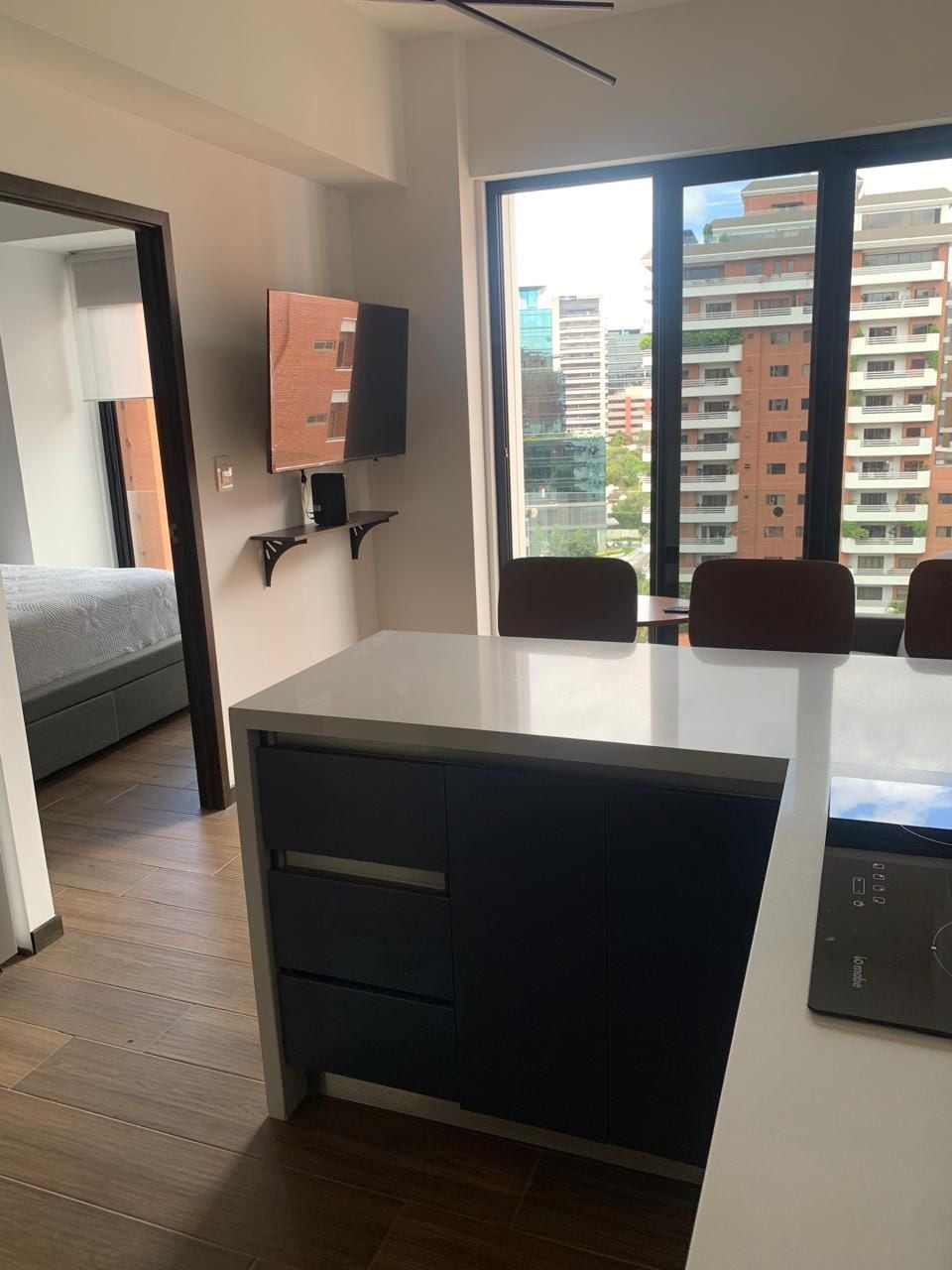 Cozinha moderna com fogão embutido, área de refeições com mesa e cadeiras, e uma janela grande com vista para a cidade.