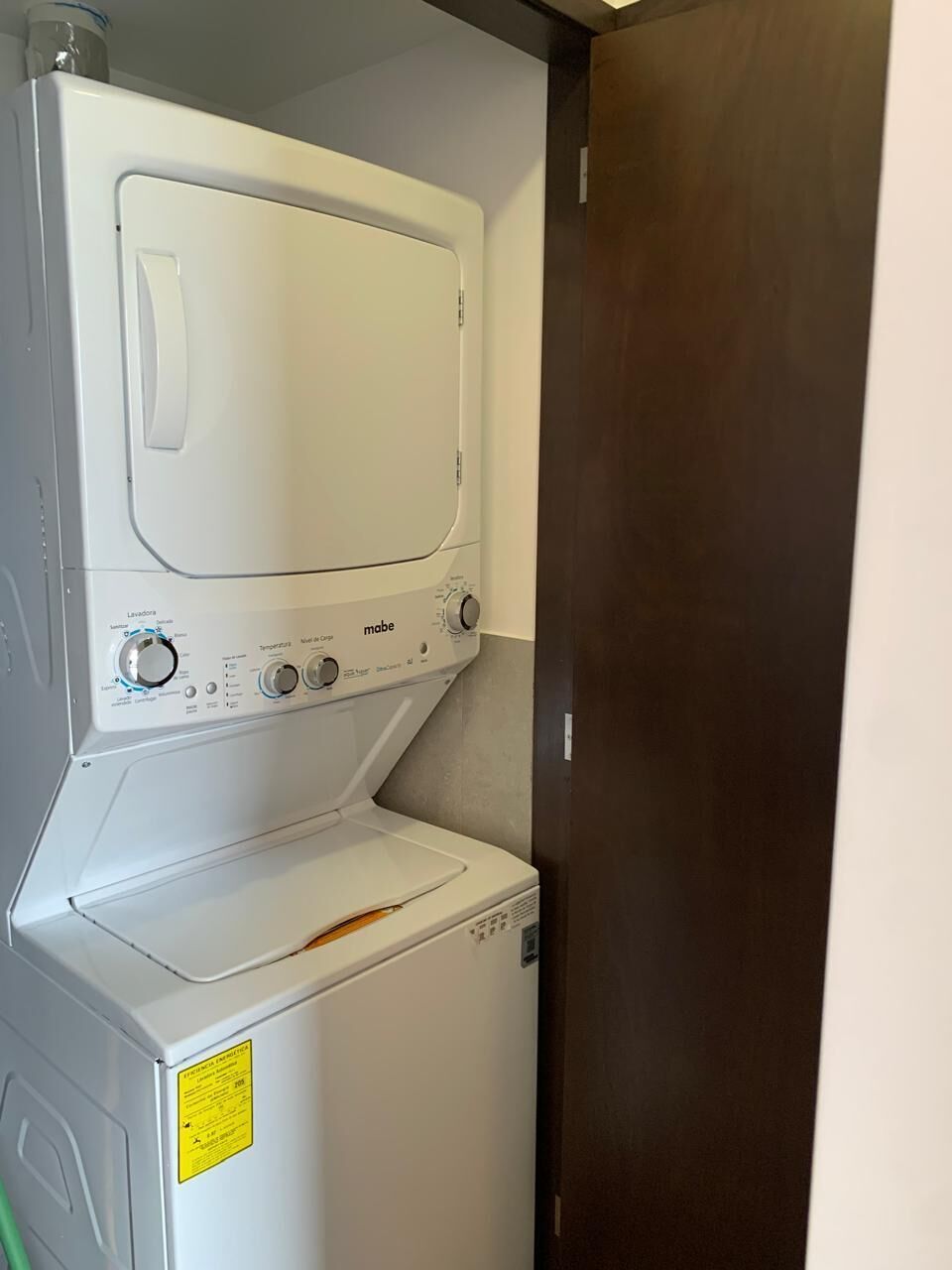 Une machine à laver et un sèche-linge blancs, placés l’un sur l’autre dans un coin, avec une porte en bois à proximité.