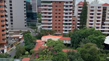 A high-rise residential building with multiple balconies, surrounded by greenery and other buildings.