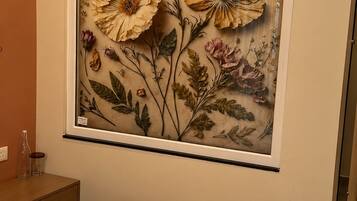 A bedroom with a bed, an air conditioning unit, and a framed floral artwork on the wall.