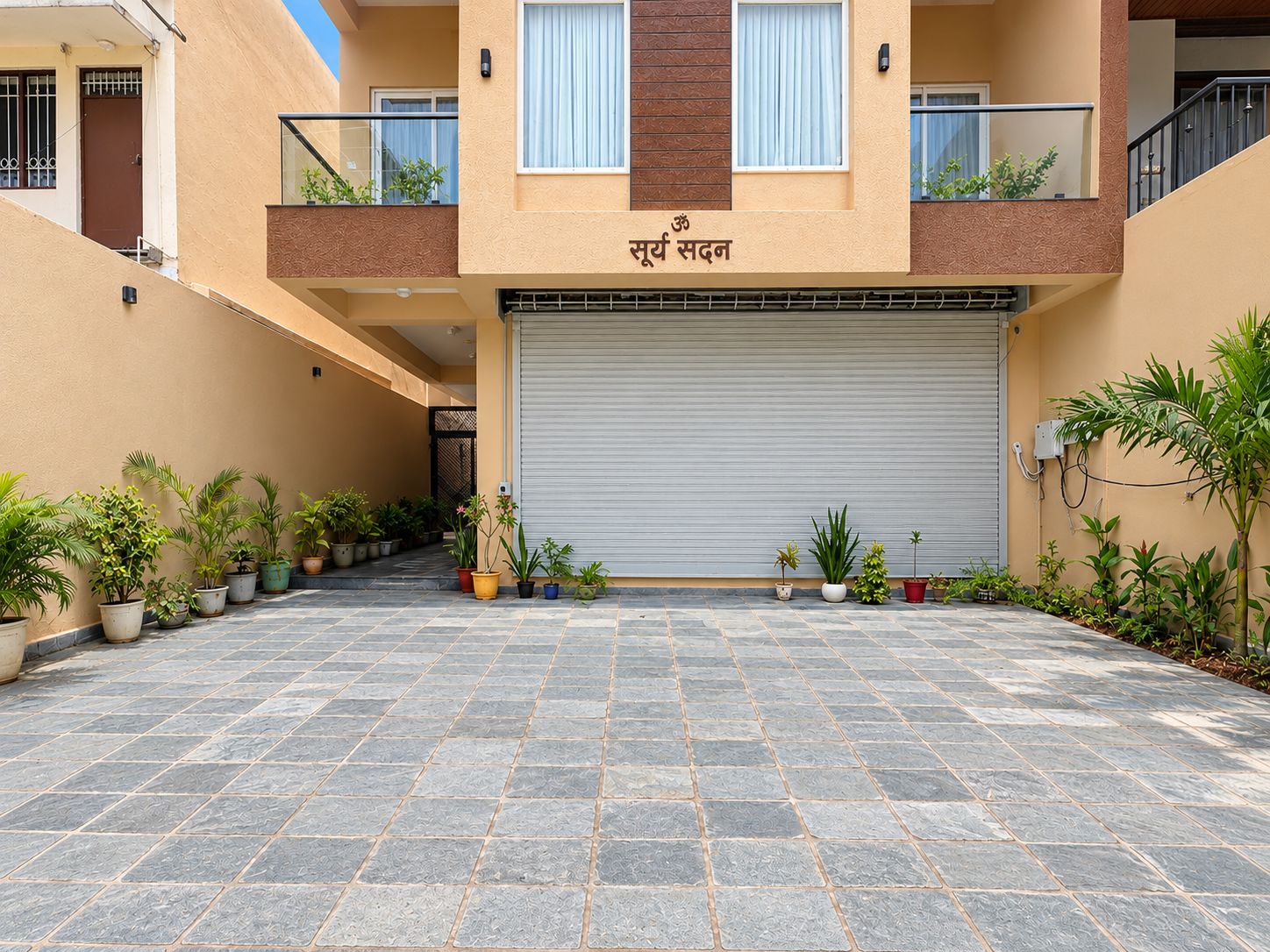 A building with a closed garage door, potted plants, and a tiled courtyard.