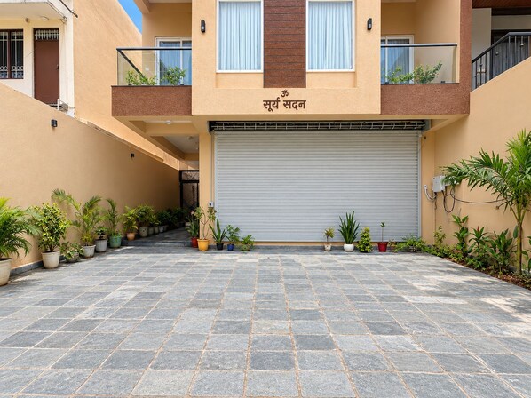 A building with a closed garage door, potted plants, and a tiled courtyard.