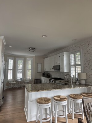 A kitchen with white cabinetry, a granite countertop, and three wicker stools. - Charming Lake Oconee Cottage- 3 Bedroom Retreat in Reynolds (Eatonton)