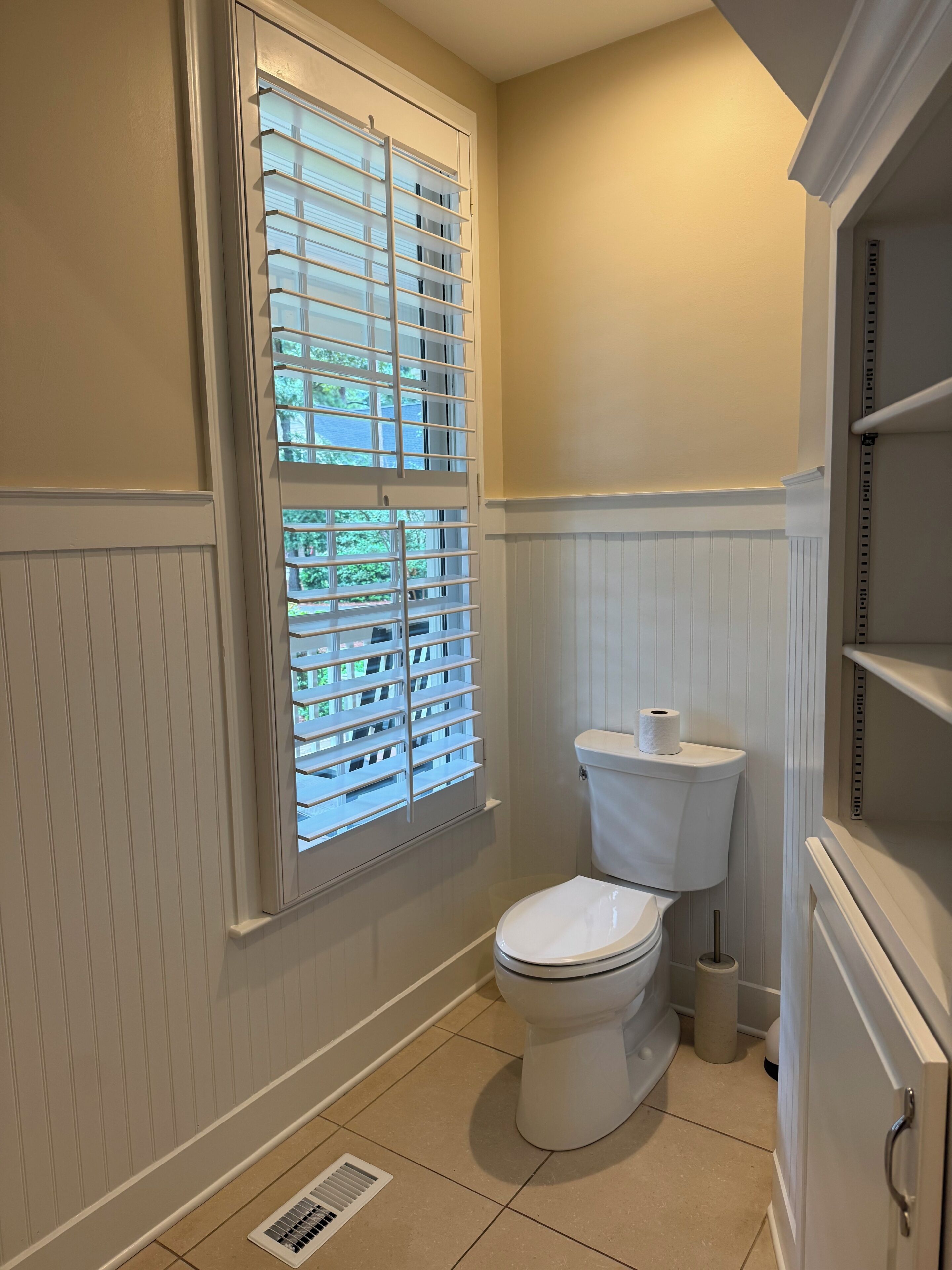 A bathroom with a toilet, a window with blinds, and a vent.