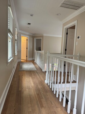 A hallway with wooden flooring, white railings, and a door leading to another room. - Charming Lake Oconee Cottage- 3 Bedroom Retreat in Reynolds (Eatonton)