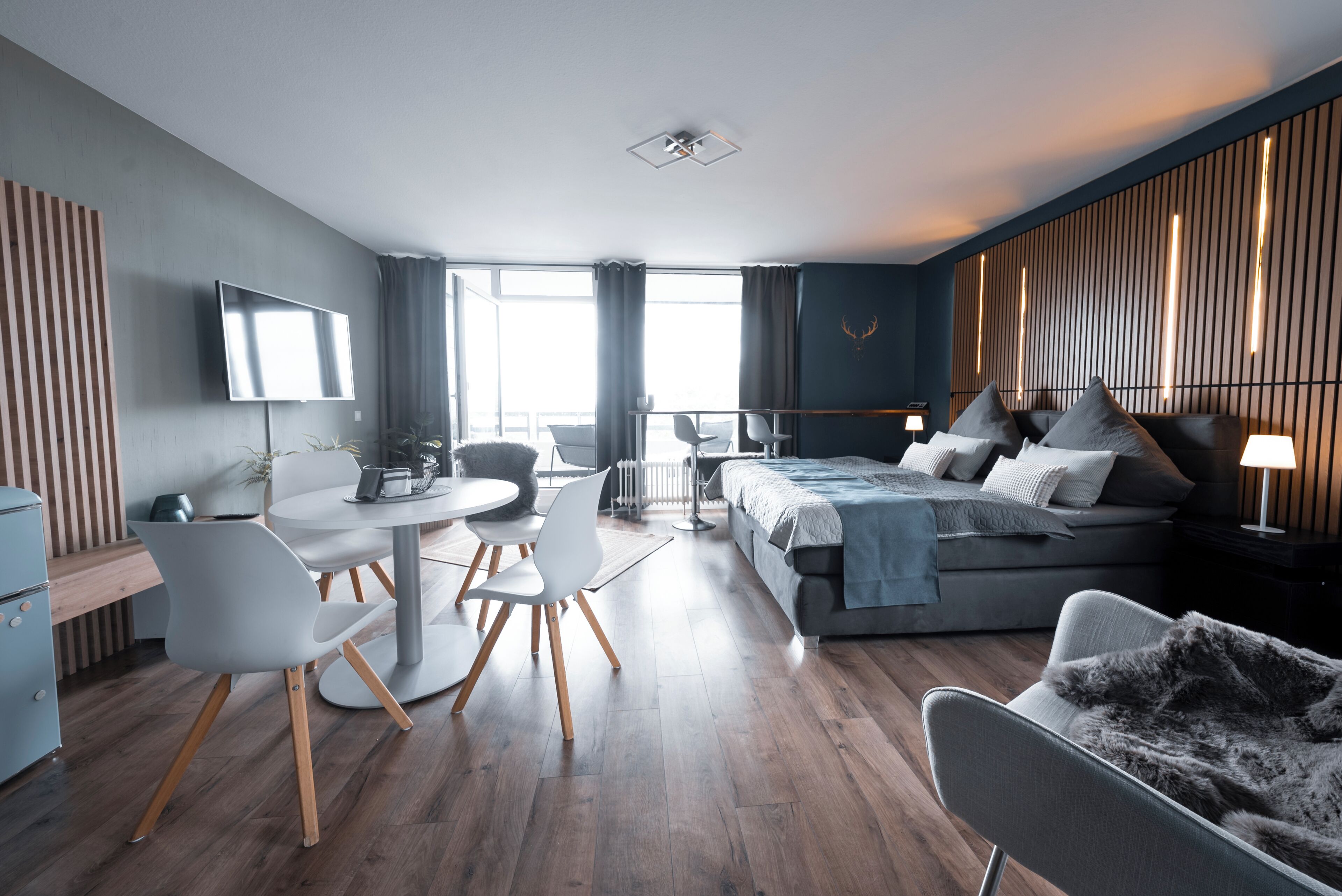 A modern hotel room with a bed, seating area, and a TV.