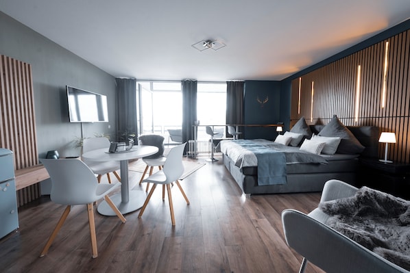 A modern hotel room with a bed, seating area, and a TV.