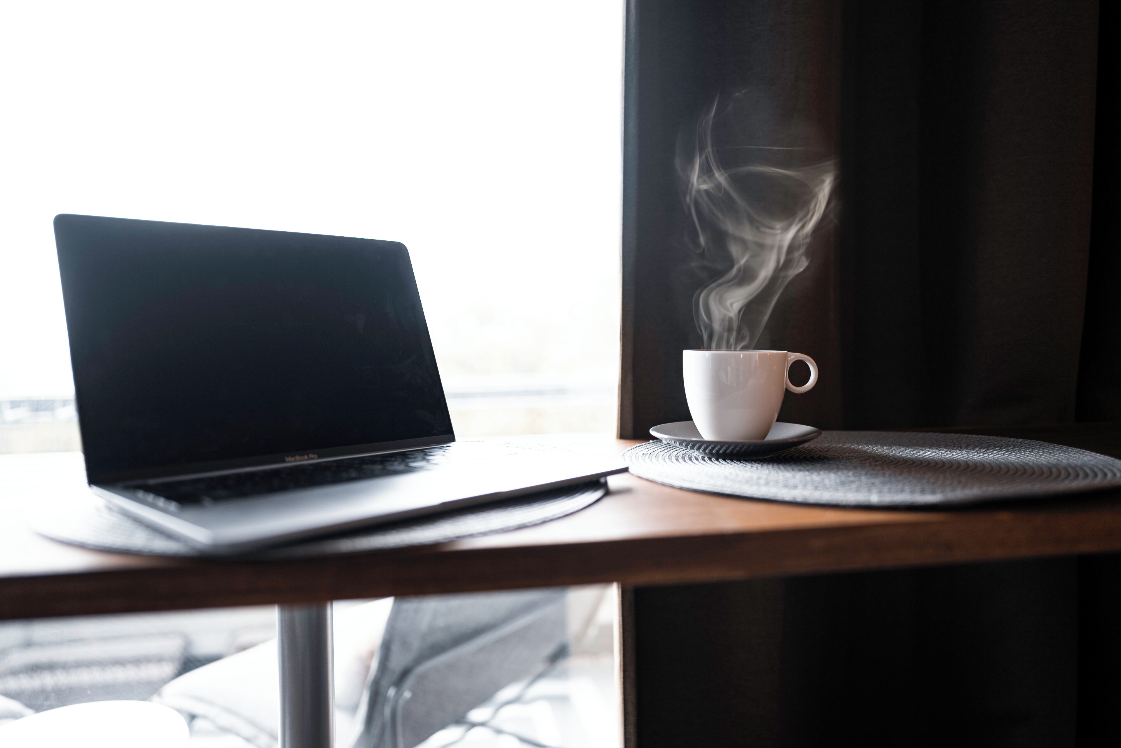 En bærbar computer på et bord med en kop kaffe, hvor der stiger damp op, der signalerer en varm drik.
