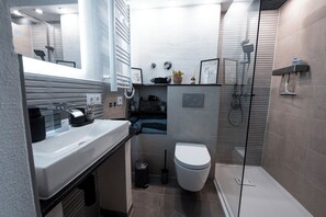 A modern bathroom with a large mirror, a sink, a toilet, and a shower area. - Vrbo Property (Linz am Rhein)