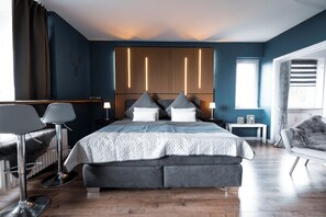 A modern bedroom with a large bed, a sitting area with a chair, and a window with curtains. - Vrbo Property (Linz am Rhein)