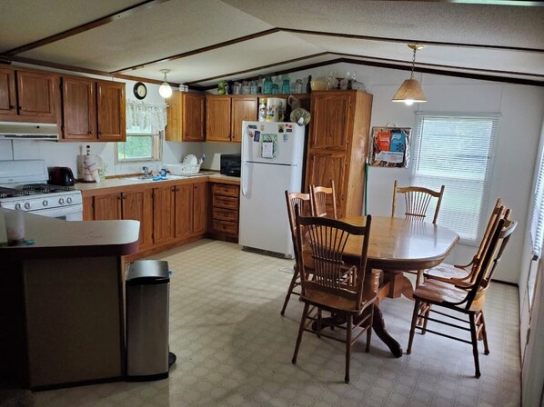 A compact kitchen with wooden cabinets, a dining table with chairs, a refrigerator, and a stove.