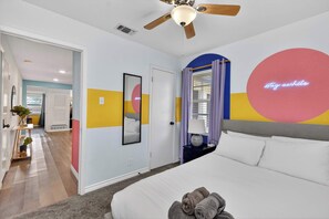 A bedroom with a bed, a ceiling fan, a mirror, and a wall with a circular design. - Modern NRH Retreat | Pool, BBQ & Sleeps 10 (Fort Worth)