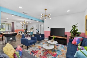 A modern living room with a foosball table, sofas, a TV, and a colorful rug.
