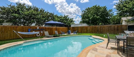 A backyard with a swimming pool, a wooden fence, and outdoor furniture.