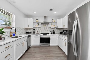 A modern kitchen with white cabinets, a stainless steel refrigerator, and a central stove.